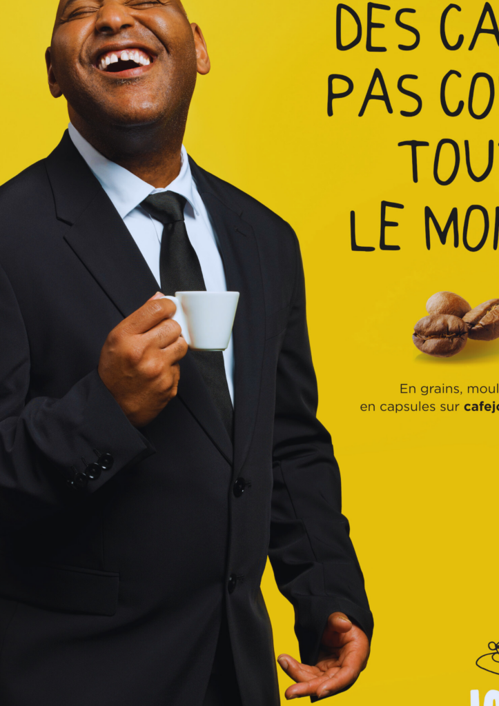 Portrait d'un équipier de Café Joyeux en costume tenant une tasse de café, sur fond jaune vif avec texte promotionnel.
